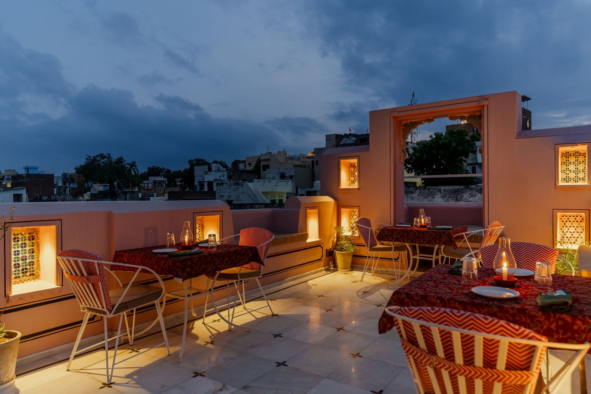 Terraza exterior con mesas y sillas, vista del paisaje urbano e iluminación decorativa.