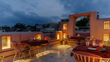 Terraza exterior con mesas y sillas, vista del paisaje urbano e iluminación decorativa.