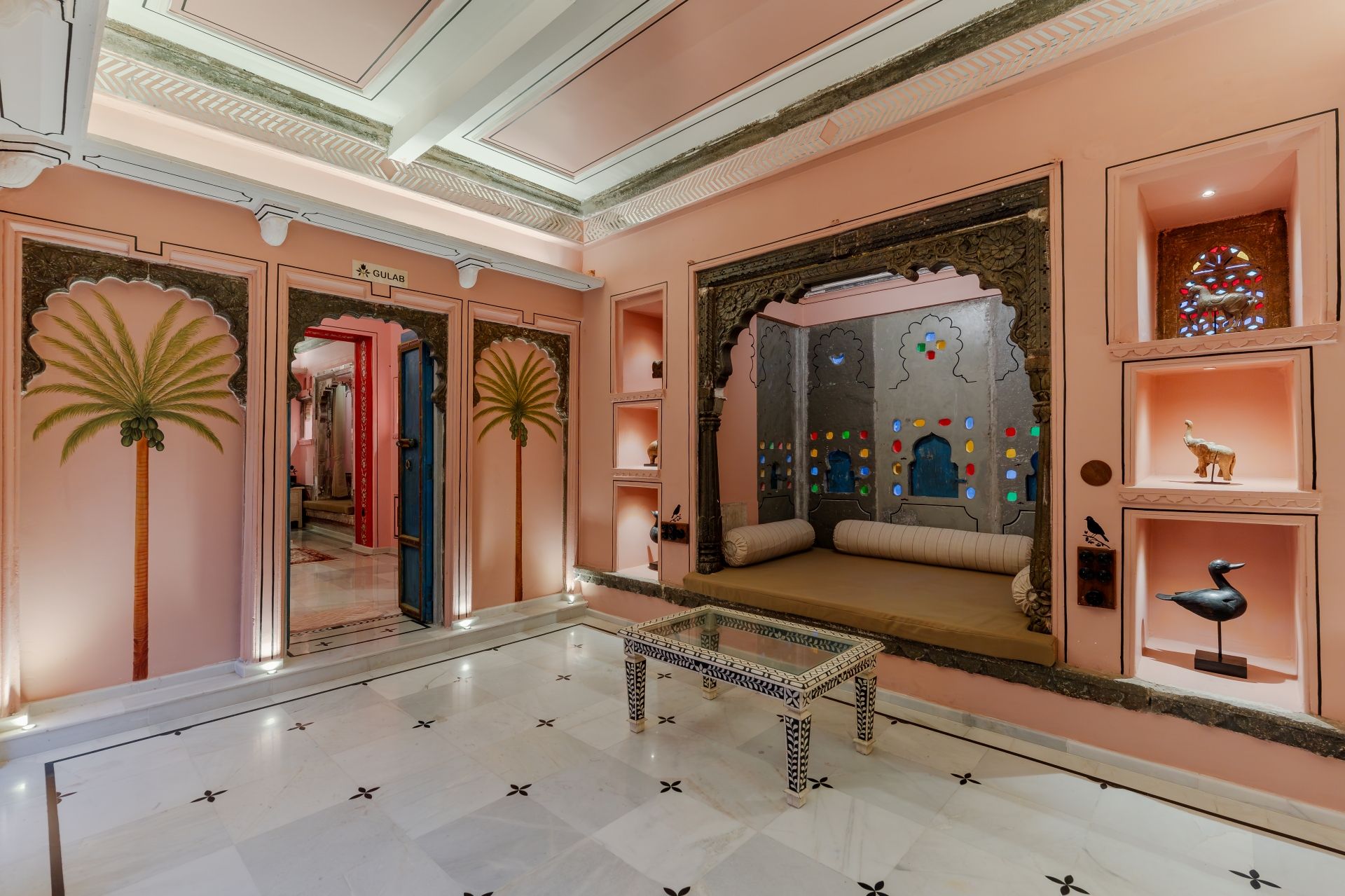 Een hotel lobby met een marmeren vloer, een centraal zitgedeelte en decoratieve elementen zoals palmstruiken en een muur met kleurrijke glazen panelen.