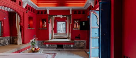A room with red walls, a large bed, a chandelier, and a view of the street.
