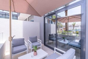 A modern outdoor seating area with a glass partition, white furniture, and a potted plant. - Stylish Studio with direct Pool Access (Jumeirah Village Circle (JVC))