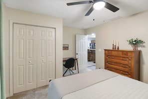 A bedroom with a bed, a dresser, a ceiling fan, and a door leading to another room.