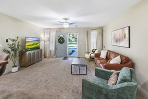 A living room with a television, a sofa, a coffee table, and a ceiling fan.