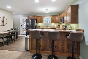 A modern kitchen with wooden cabinets, a stainless steel refrigerator, a microwave, and a bar area with stools.