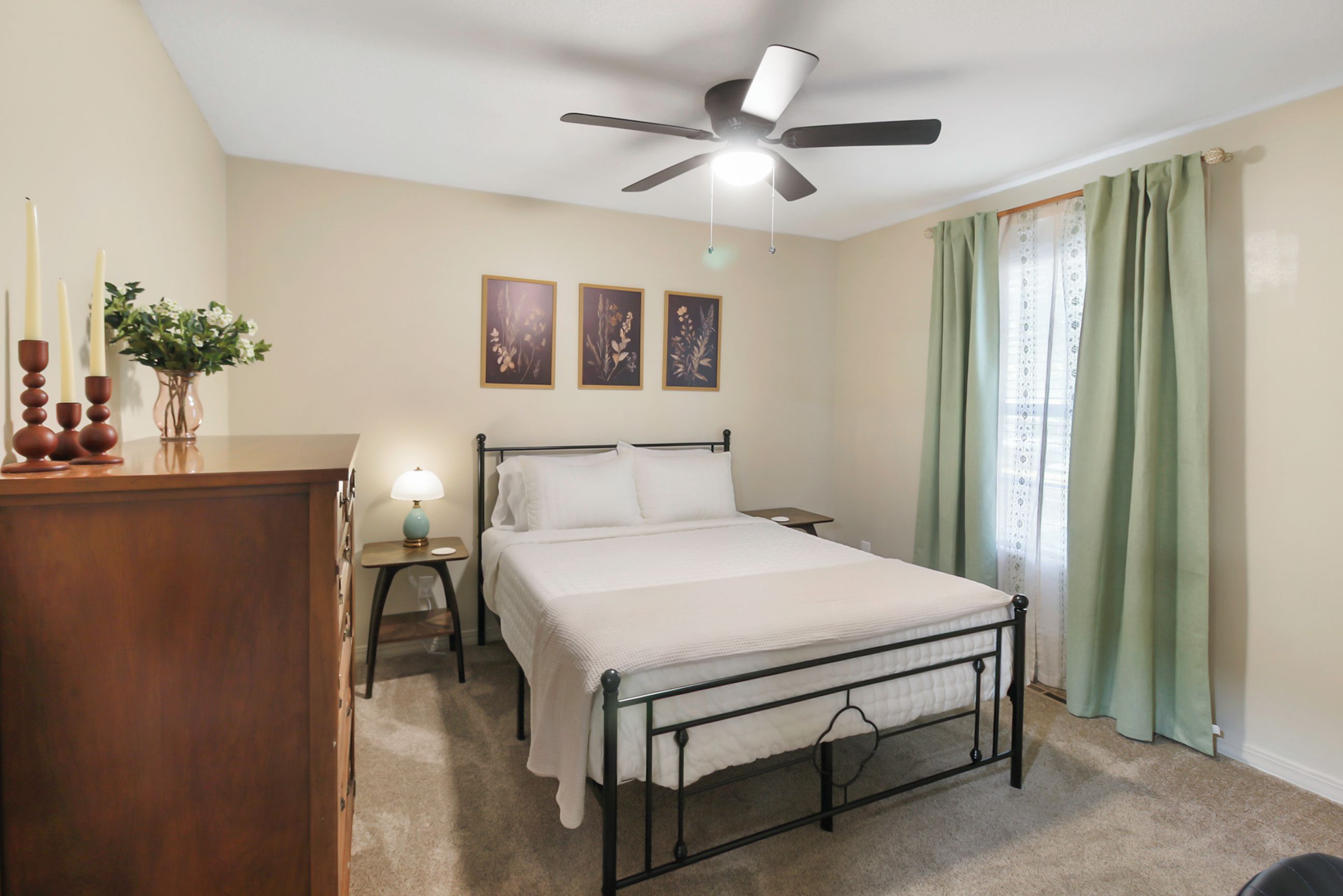 A bedroom with a bed, a nightstand, a lamp, a ceiling fan, and a window with curtains.