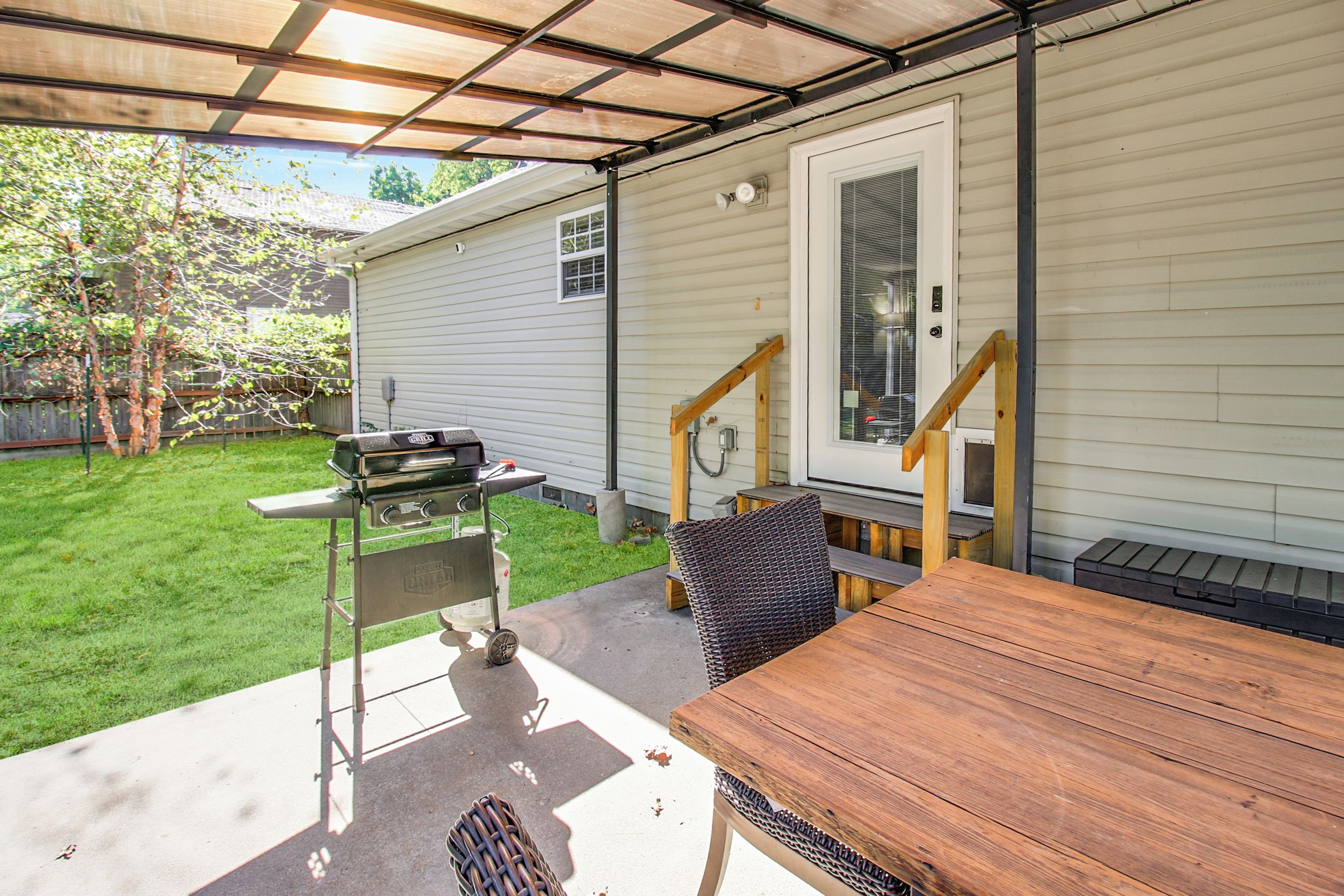 A covered patio area with a grill, a table, and a chair.