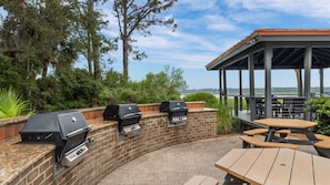 Une terrasse extérieure avec des murs en briques, trois barbecues et des tables de pique-nique en bois.