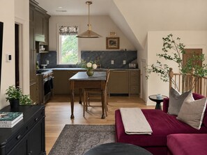 A modern kitchen with a dining table and chairs, a red sofa, and a small side table with a plant. - Maplewood Cottage • Heated Pool, Hot Tub, Gym, Grill, Fire Pit (Nashville)