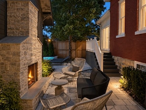 A stone fireplace, outdoor seating with wicker chairs, and a wooden deck. - Maplewood Cottage • Heated Pool, Hot Tub, Gym, Grill, Fire Pit (Nashville)