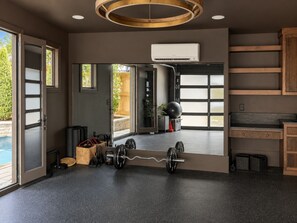A modern gym with a weightlifting area, a large mirror, and a view of the outdoors. - Maplewood Cottage • Heated Pool, Hot Tub, Gym, Grill, Fire Pit (Nashville)