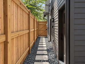 A narrow pathway flanked by wooden fences leading to a building with a gray siding exterior. - Maplewood Cottage • Heated Pool, Hot Tub, Gym, Grill, Fire Pit (Nashville)