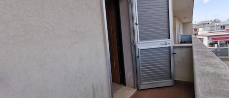 Un balcón con puerta metálica cerrada y suelo de baldosas.