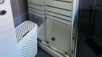 Een douchecabine met glazen wanden, een witte mand en een handdoekhouder.