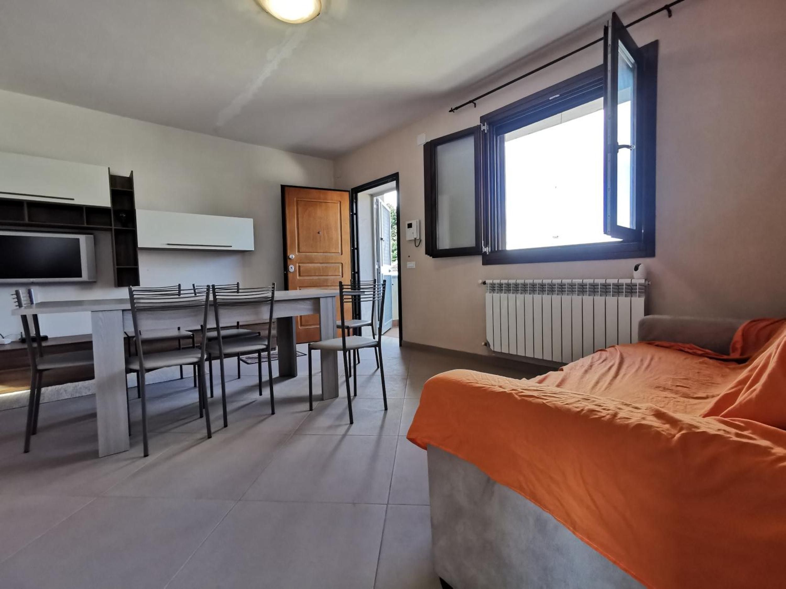 Ein gemütlicher Raum mit Bett, Esstisch mit Stühlen, Fernseher und Fenster.