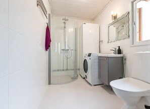Badeværelse med brusekabine i glas, vaskemaskine, toilet og spejl.