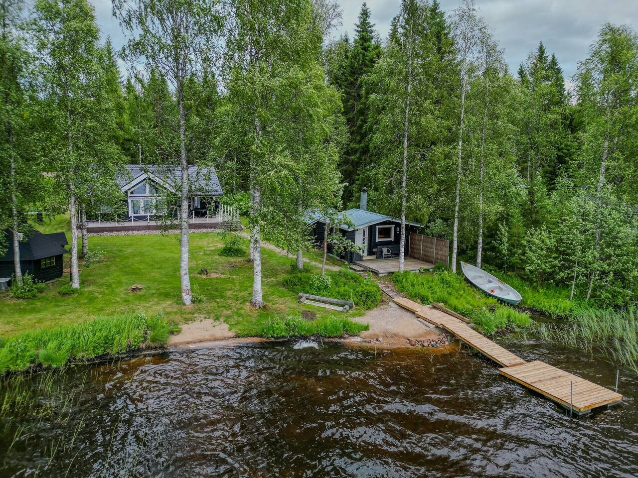 A lakeside cabin with a dock extending into the water, surrounded by dense forest.