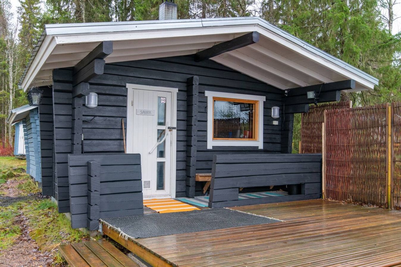 Une cabane avec une véranda, une porte et une fenêtre.