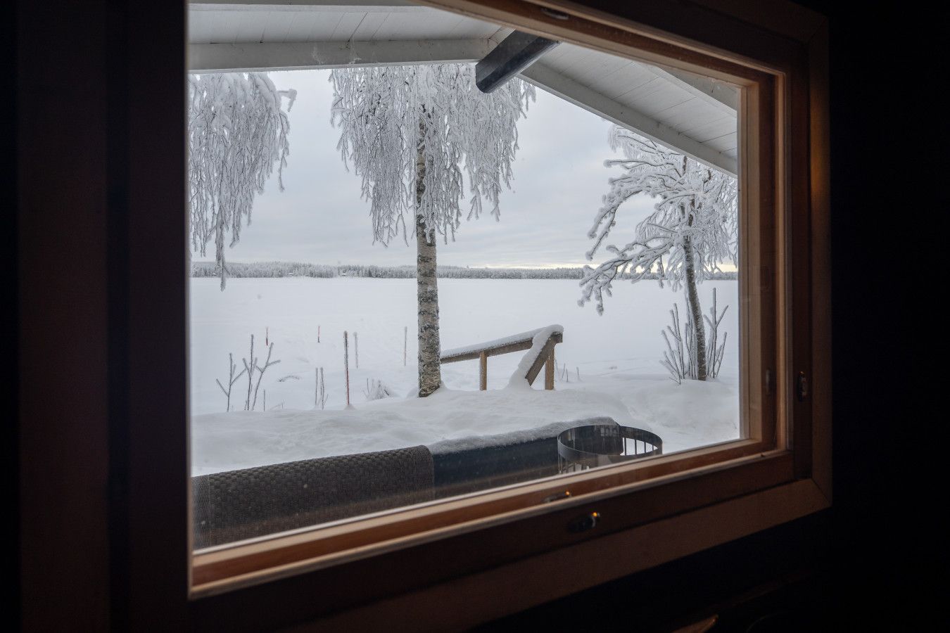 Una ventana con vista a un paisaje nevado, que incluye un banco y árboles.