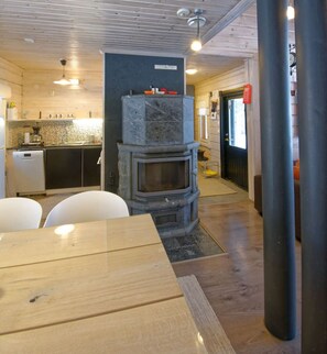 A modern kitchen with a built-in stone fireplace, wooden cabinets, and a dining area with a table and chairs.