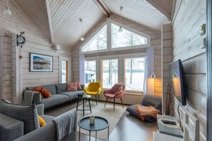 Ein gemütliches Interieur mit einer Couch, Sesseln, einem Fernseher und einem großen Fenster mit Blick nach draußen.