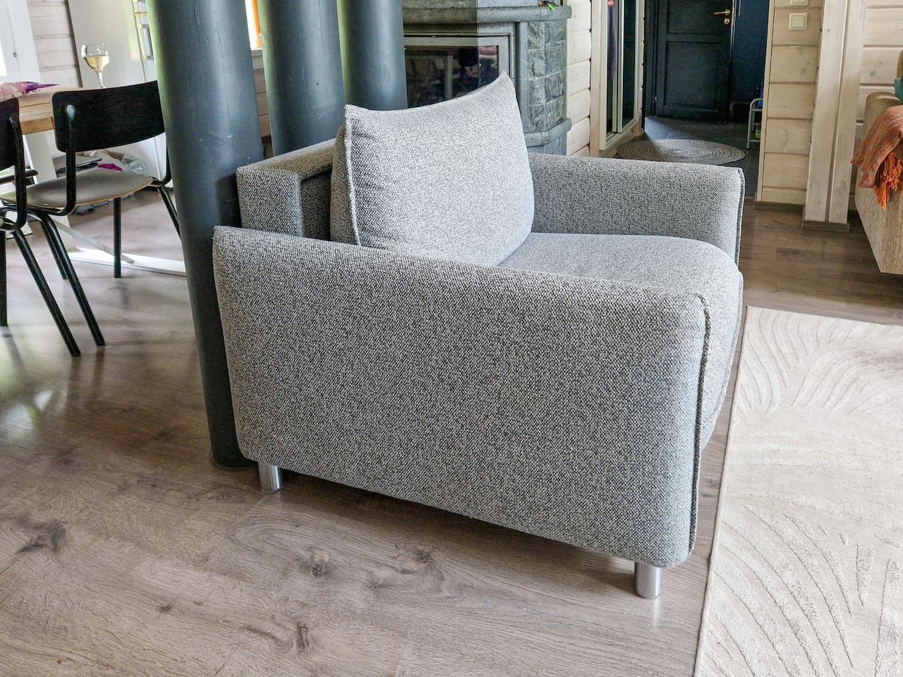 Un canapé gris, recouvert d’un tissu texturé, est placé dans une pièce dont le sol est en bois et qui est agrémentée d’un tapis à motifs.