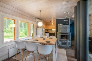 Et træinteriør med spiseområde, køkken og pejs.
