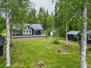A house with a deck, surrounded by a grassy yard and trees.
