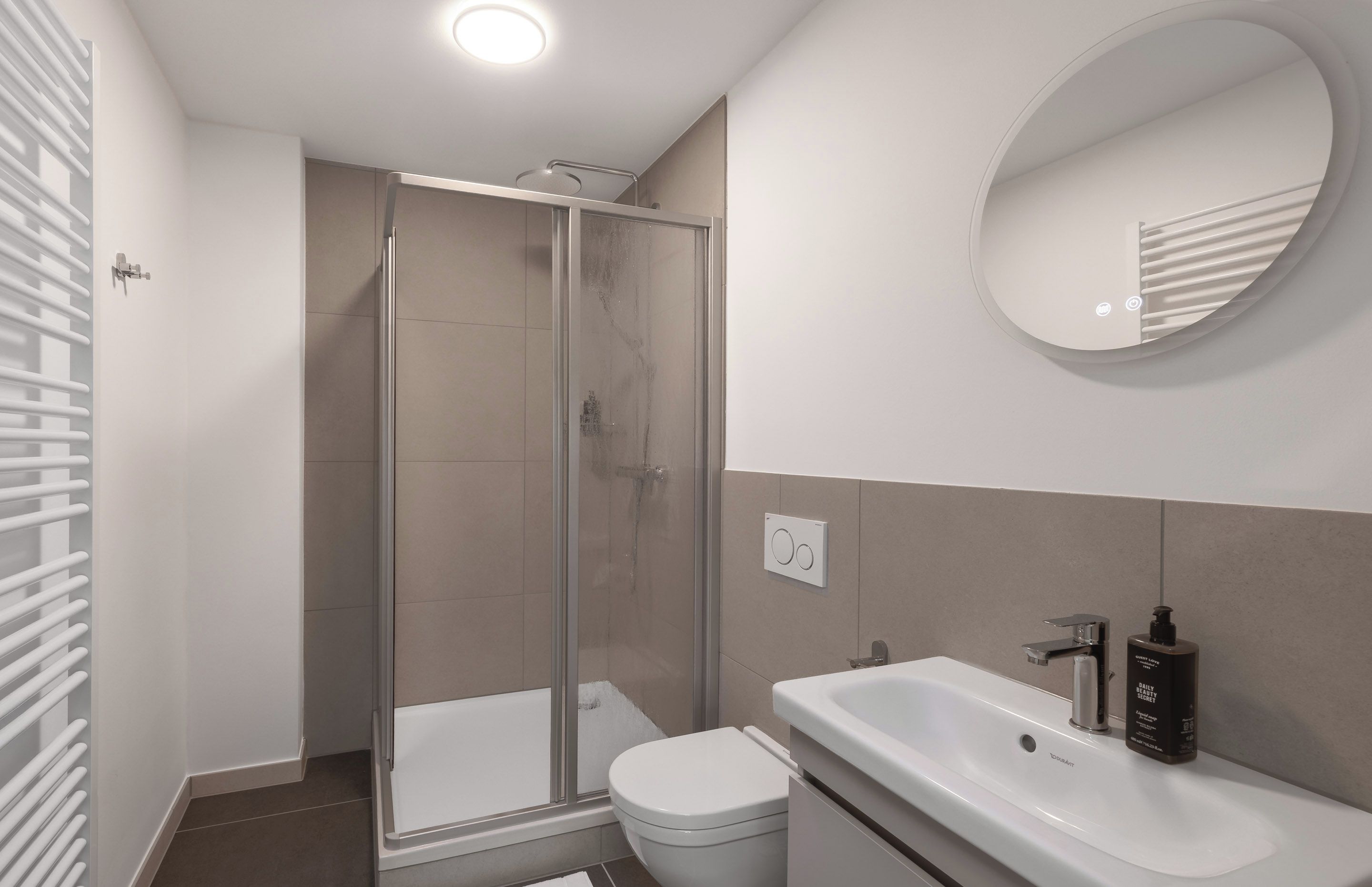 A modern bathroom with a glass shower enclosure, a white toilet, a sink with a soap dispenser, and a mirror above the sink.