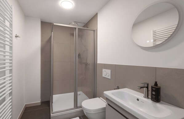 A modern bathroom with a glass shower enclosure, a white toilet, a sink with a soap dispenser, and a mirror above the sink.