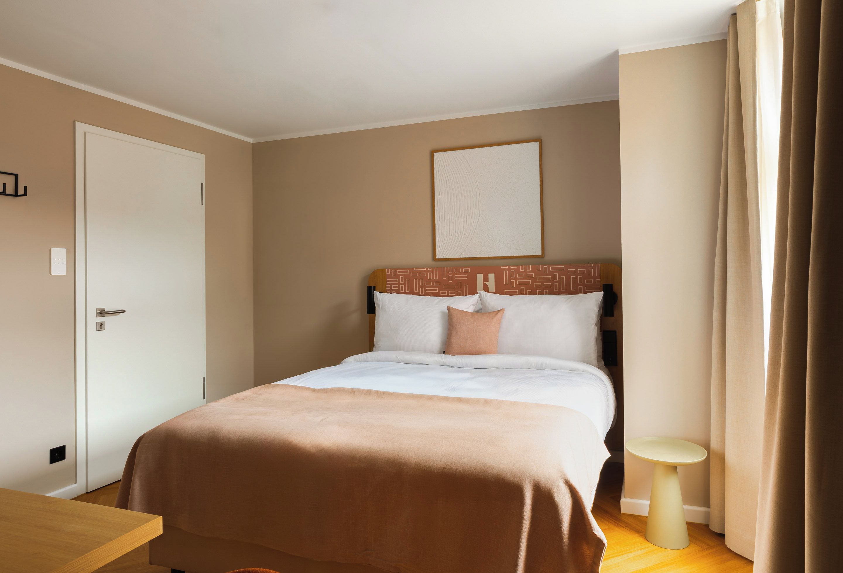 A hotel room with a bed, bedside table, and a small round table.