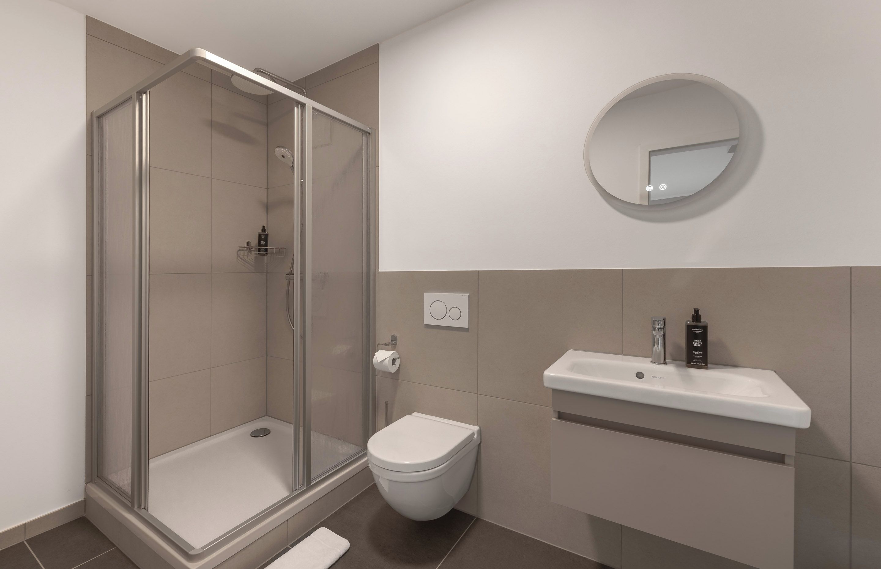 Un baño moderno con cabina de ducha de vidrio, inodoro blanco y tocador con espejo.