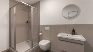 Un baño moderno con cabina de ducha de vidrio, inodoro blanco y tocador con espejo.
