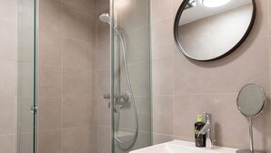 Un bany modern amb dutxa de vidre, un mirall rodó i un lavabo amb dosificador de sabó.