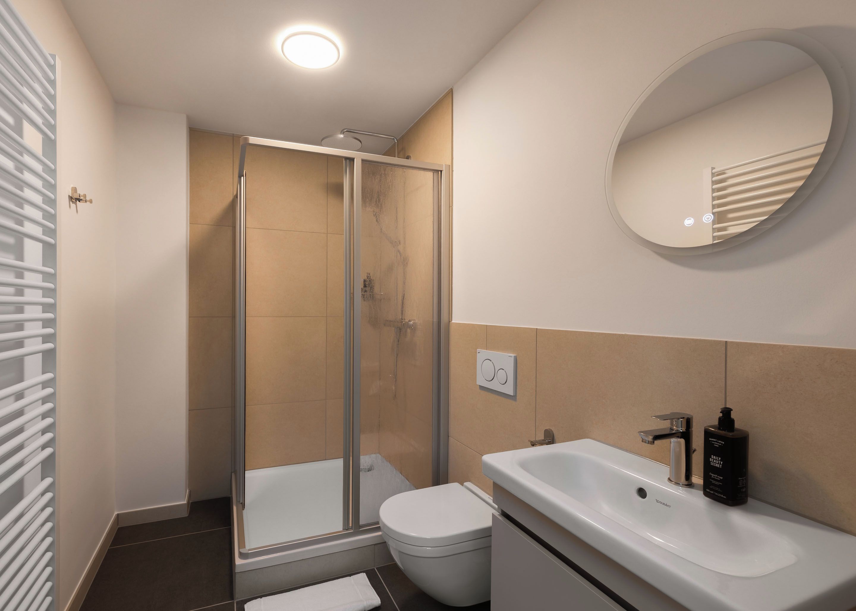 Un baño moderno con ducha envuelta en vidrio, inodoro blanco, lavamanos con dispensador de jabón y un espejo en la pared.