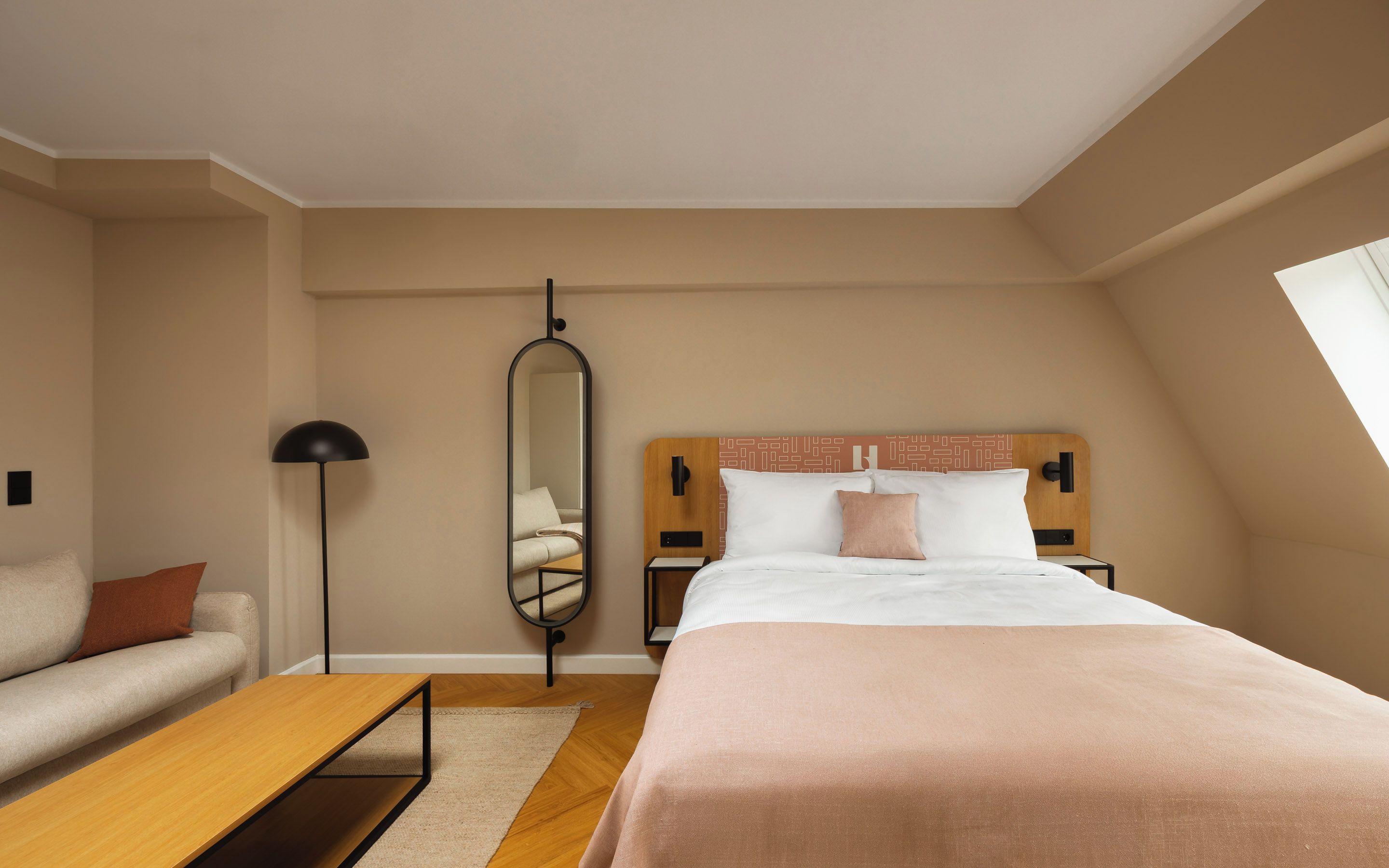 A bedroom with a bed, a sofa, a mirror, a nightstand, and a lamp.