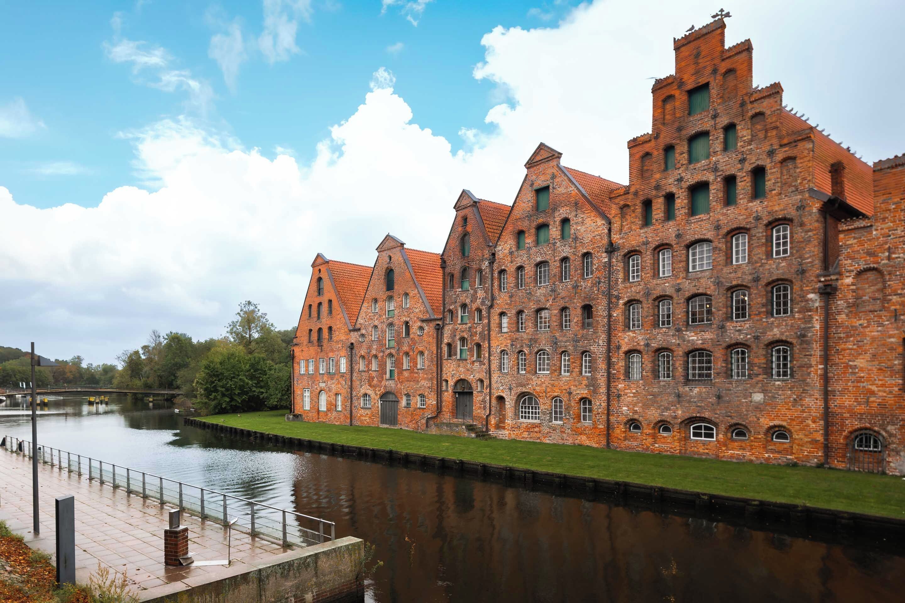 A large brick building with multiple windows and a river in the foreground.