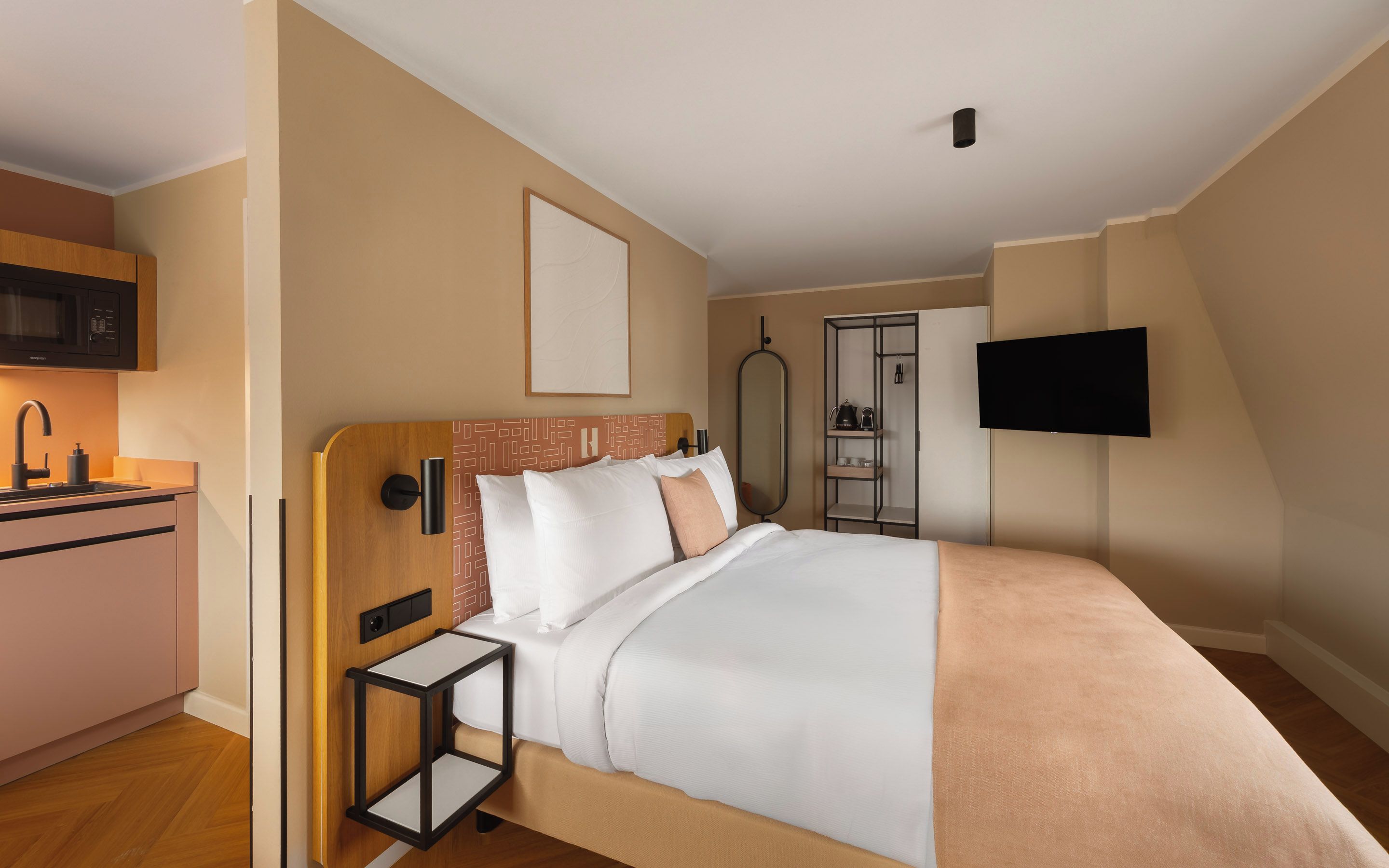 A hotel room with a bed, a bedside table, a TV, a wardrobe, and a kitchenette.