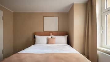 Ein Hotelzimmer mit einem Bett, einem Kopfteil mit geometrischem Muster, einer schlichten Wand und einem Fenster mit Vorhängen.