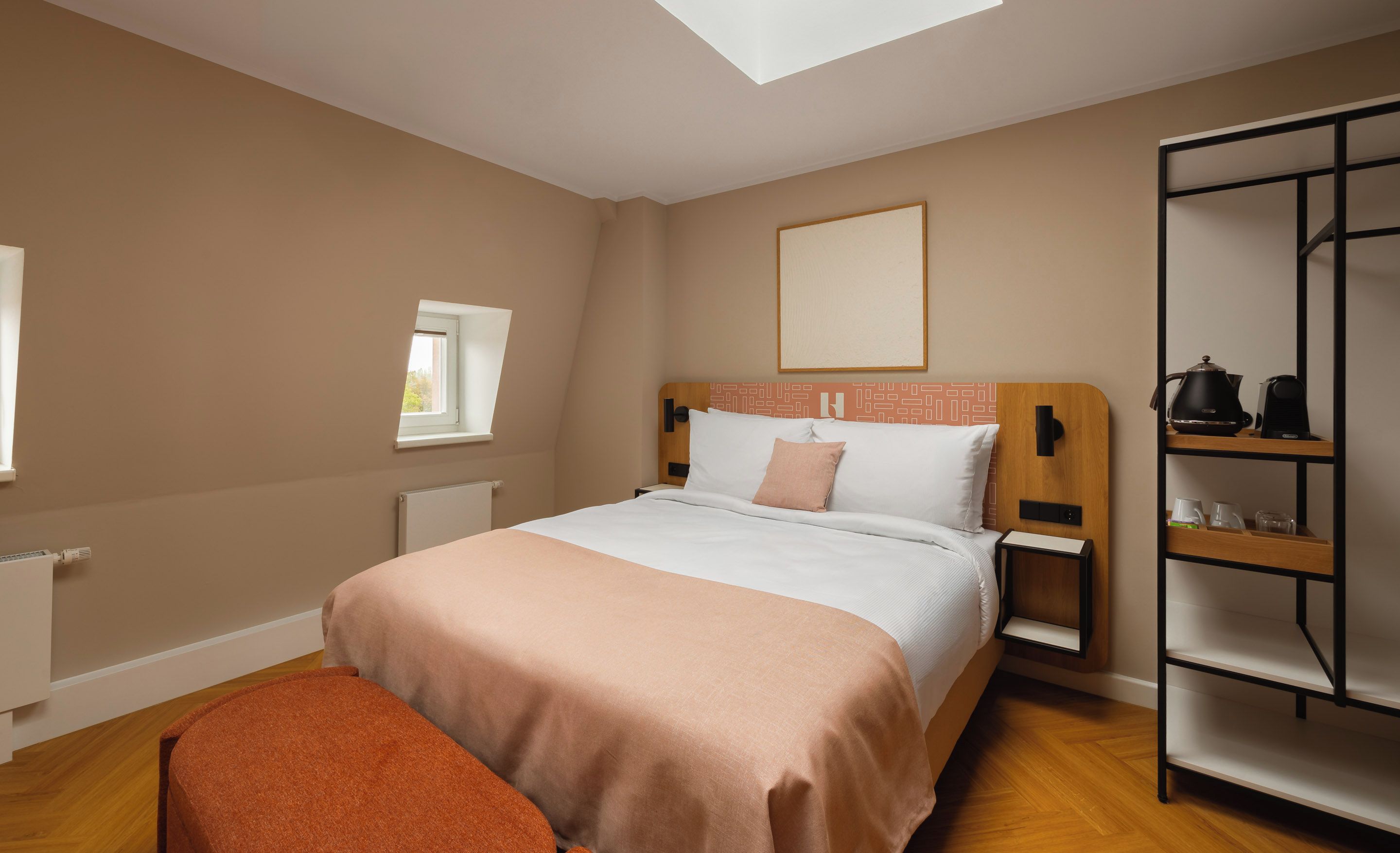 Ein Schlafzimmer mit einem Bett, einem Nachttisch, einem Heizkörper, einem Fenster, einem Regal mit Küchenutensilien und einer Bank.