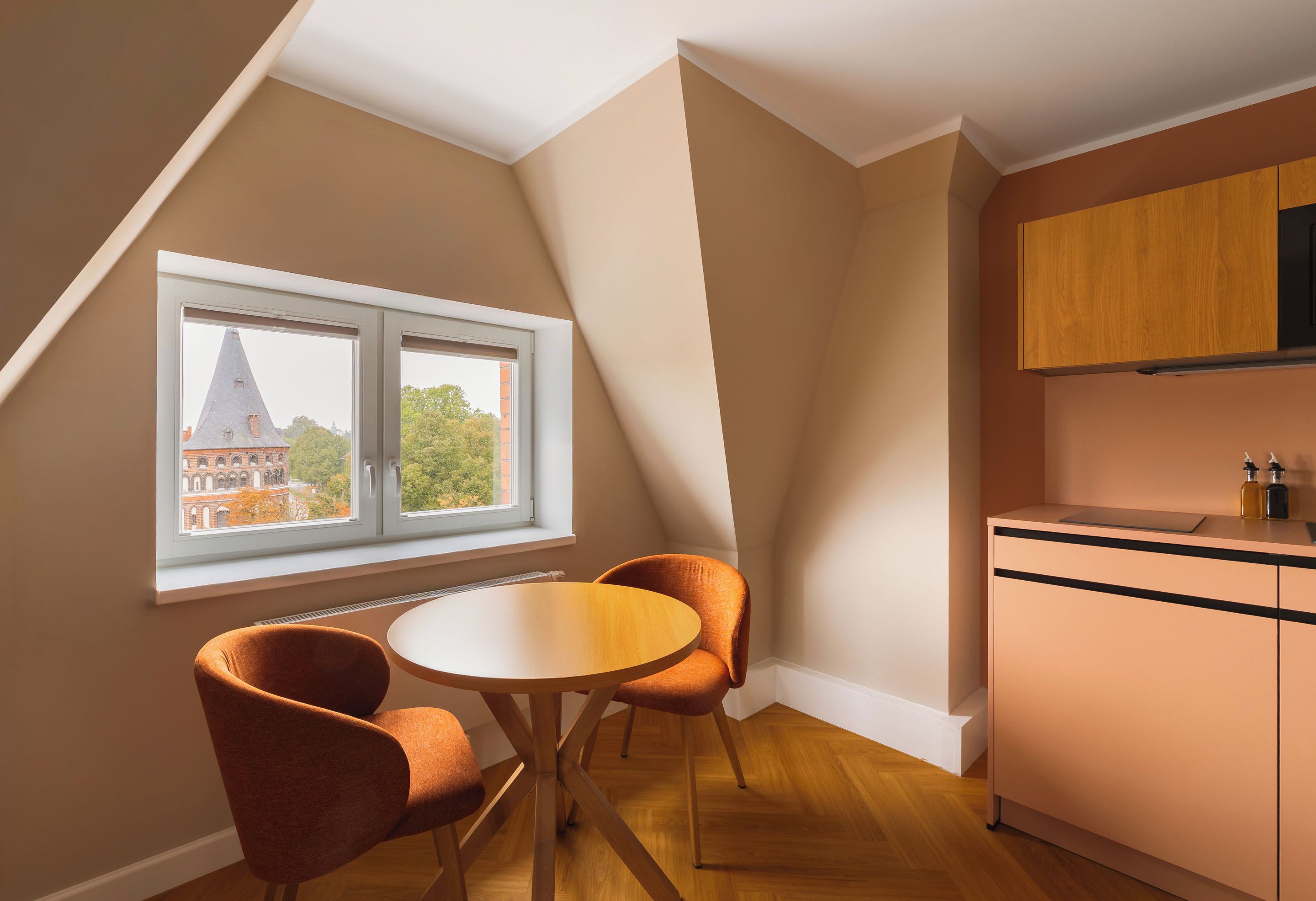 Ein Zimmer mit Esstisch und Stühlen, ein Fenster mit Blick auf ein Gebäude und eine Küchenzeile mit Schränken.