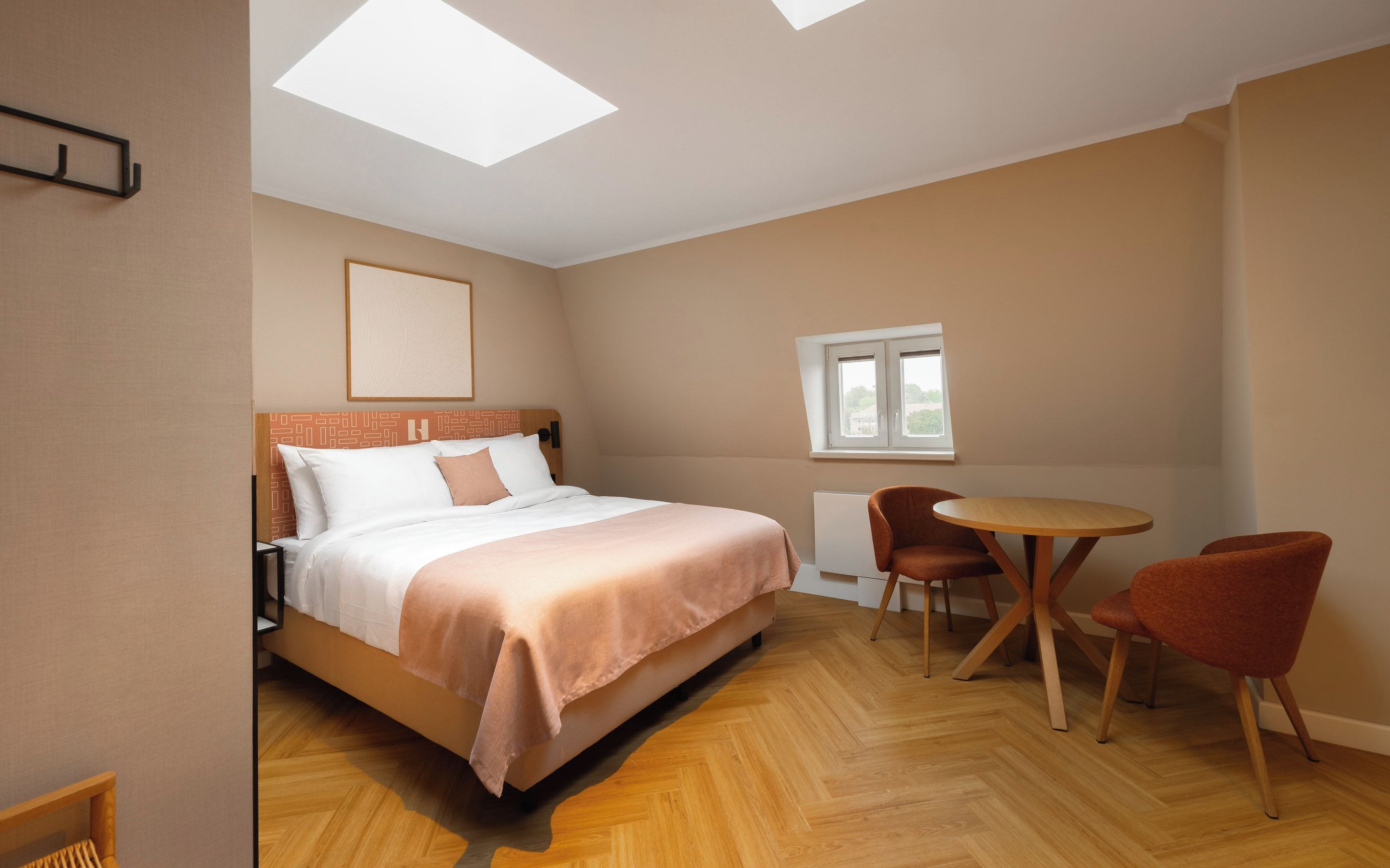 Ein Schlafzimmer mit einem Bett, einem runden Tisch, zwei Stühlen, einem Fenster und einem Oberlicht.