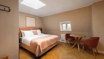 Ein Schlafzimmer mit einem Bett, einem runden Tisch, zwei Stühlen, einem Fenster und einem Oberlicht.