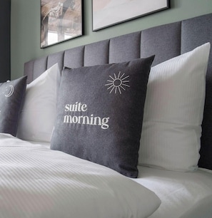 Ein Bett mit grauem Kopfteil, weißer Bettwäsche und einem Kopfkissen mit dem Aufdruck 'suite morning'.