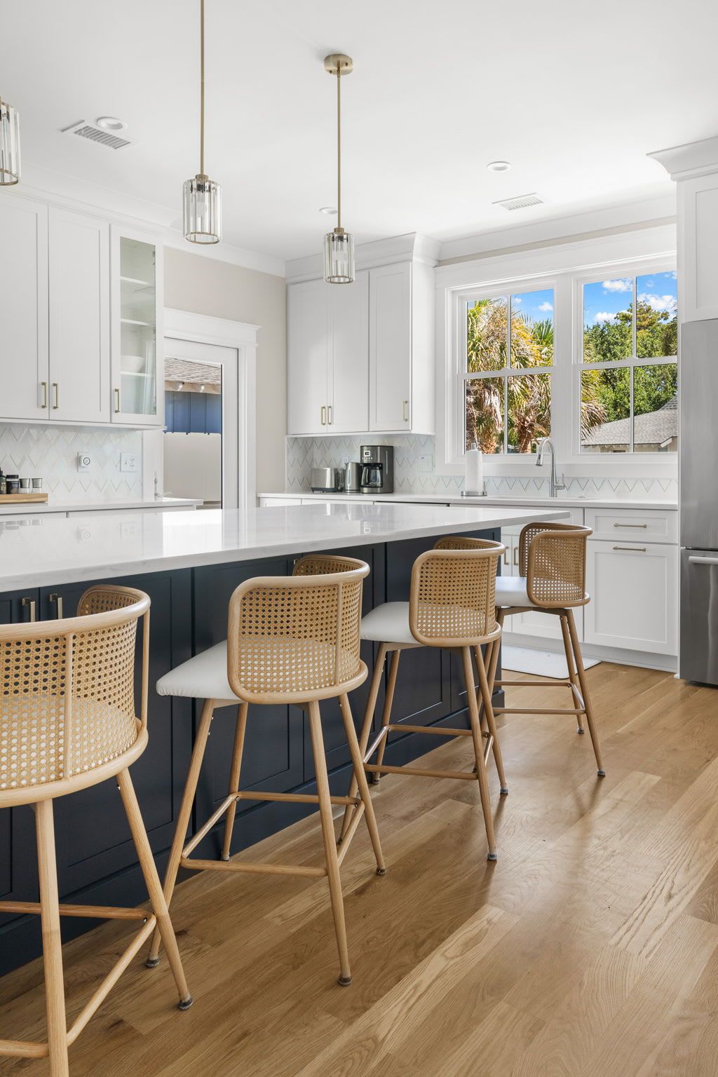 A modern kitchen with white cabinetry, a central island with bar stools, and a view of the outdoors.