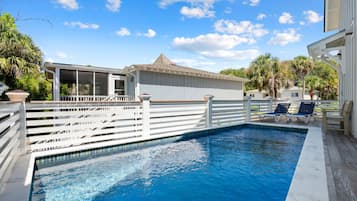 A swimming pool with a white deck, surrounded by a white fence, and a building with a covered deck area.