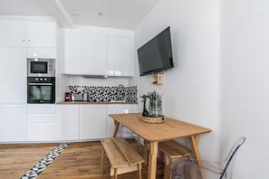 Eine kompakte Küche mit weißen Schränken, einer Mikrowelle und einem eingebauten Backofen. Ein Flachbildfernseher ist an der Wand über der Arbeitsplatte angebracht.