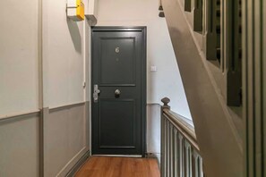 Ein schmaler Flur mit einer dunklen Tür, die mit der Nummer 6 gekennzeichnet ist, einer weißen Wand und einem Holzboden.