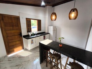 A kitchen with a marble floor, wooden stools, a black countertop, and pendant lights. - Casa no Centro Histórico de Cananéia – Perto de Tudo e da Beira-Mar (Cananéia)