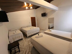 A room with three beds, a small table, a television mounted on the wall, and a wooden ceiling. - Casa no Centro Histórico de Cananéia – Perto de Tudo e da Beira-Mar (Cananéia)