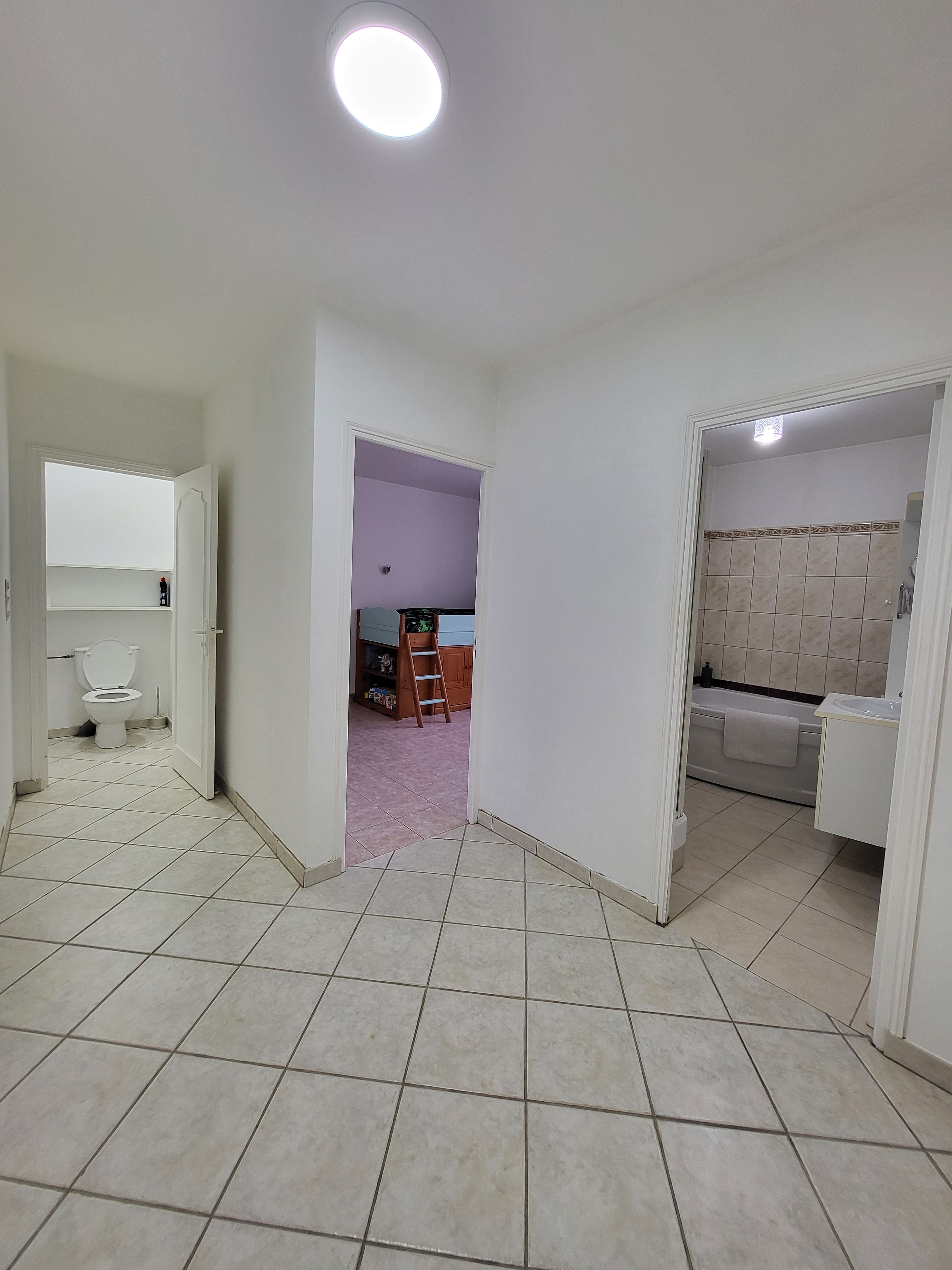 Habitación con inodoro, lavamanos y bañera. Se ve una puerta que da a otra habitación con una escalera y estantes.